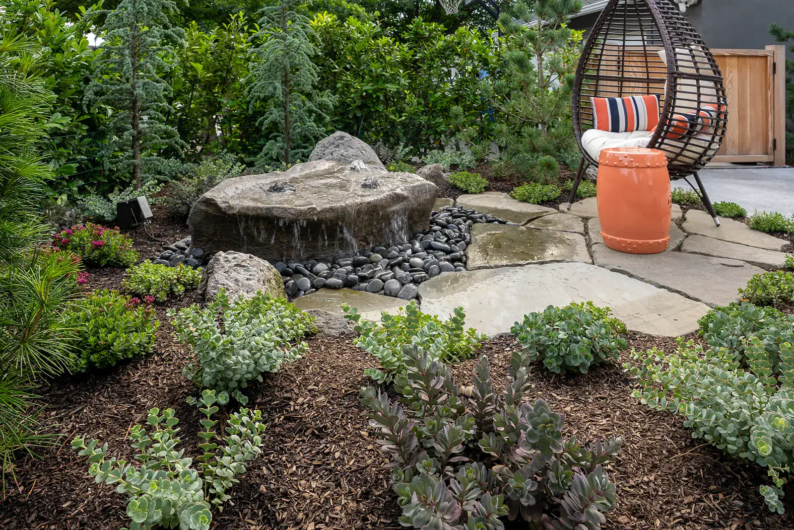 Cedar pergola post detail with steel base hardware, succulent and sedum planting pocket, concrete patio with pebble inlay, and outdoor dining space beneath custom hardscape structure