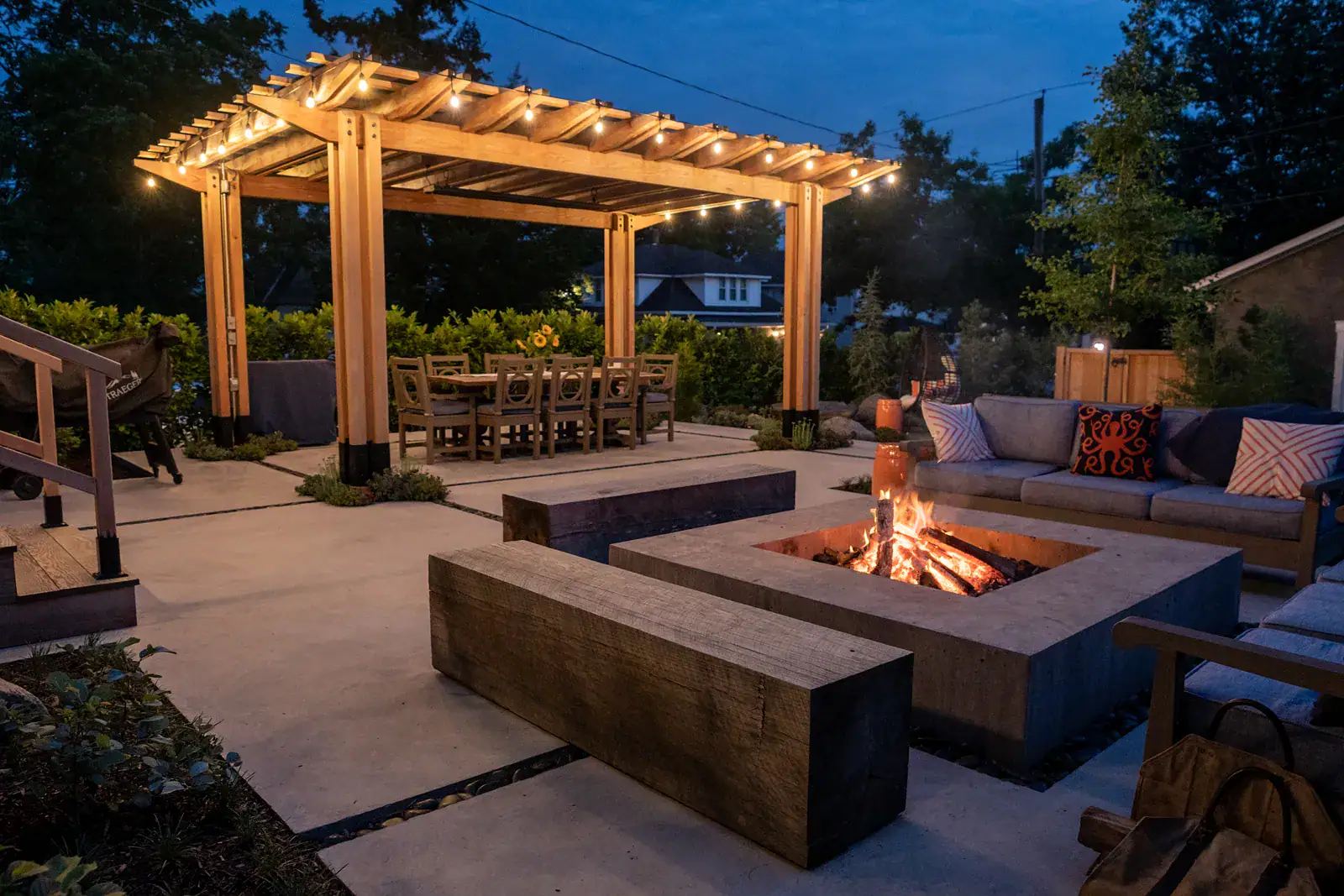 Cedar pergola post detail with steel base hardware, succulent and sedum planting pocket, concrete patio with pebble inlay, and outdoor dining space beneath custom hardscape structure