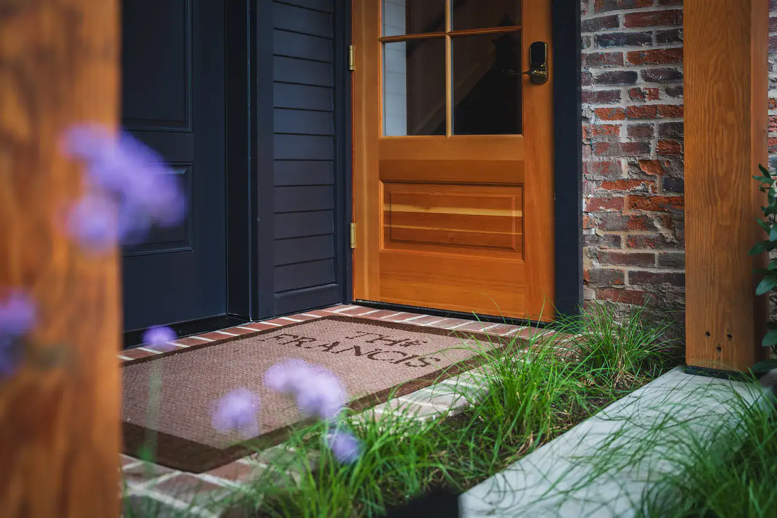 GR-FrancisHotel-08539 Open wood and glass entry door with The Francis doormat, brick surround, and ornamental grass planting along a bluestone step