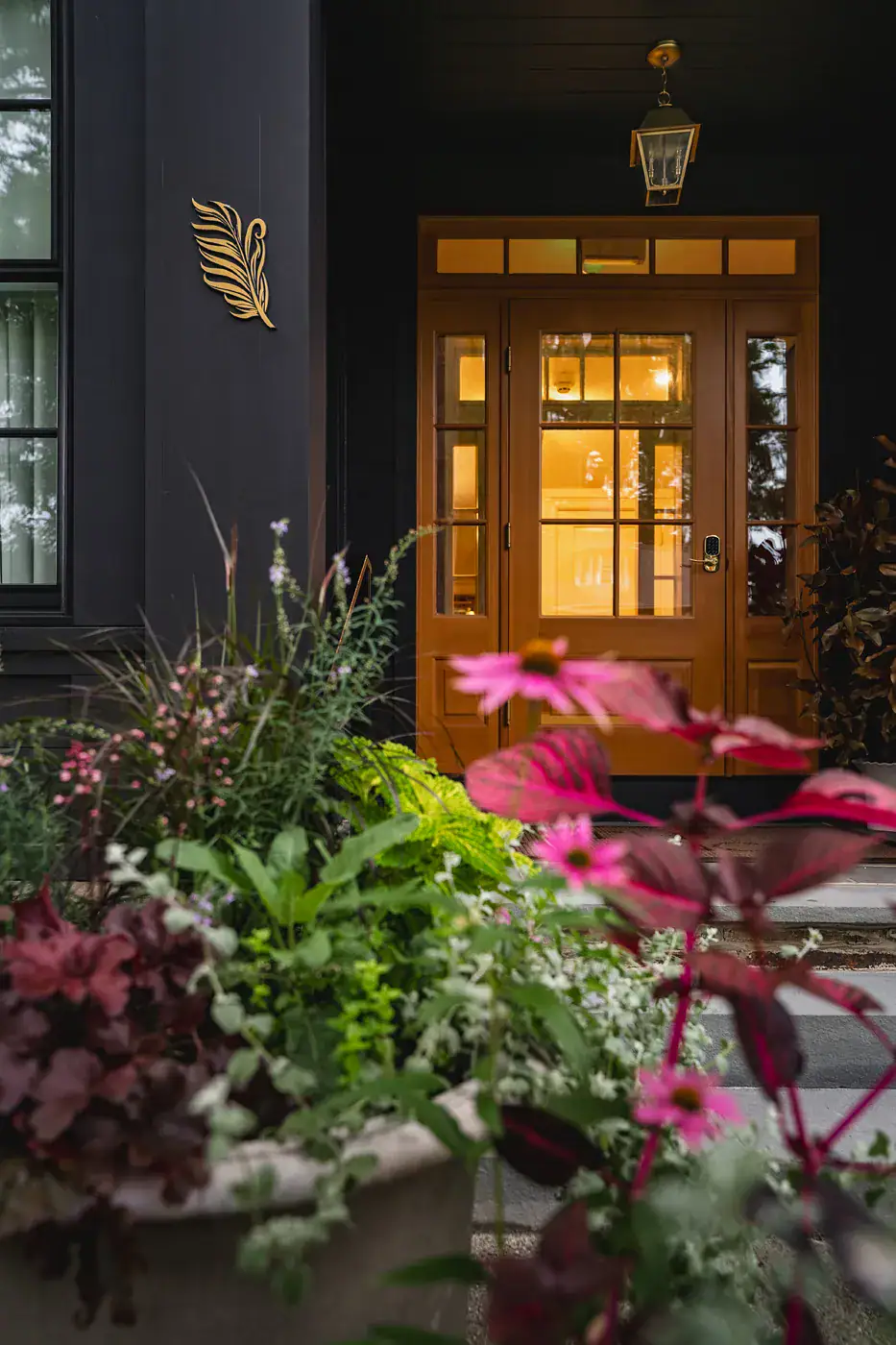 GR-FrancisHotel-08776 Warmly lit entrance of the Francis Hotel with a golden wood door, gas lantern, gold feather wall sculpture, and lush container plantings of echinacea and coleus
