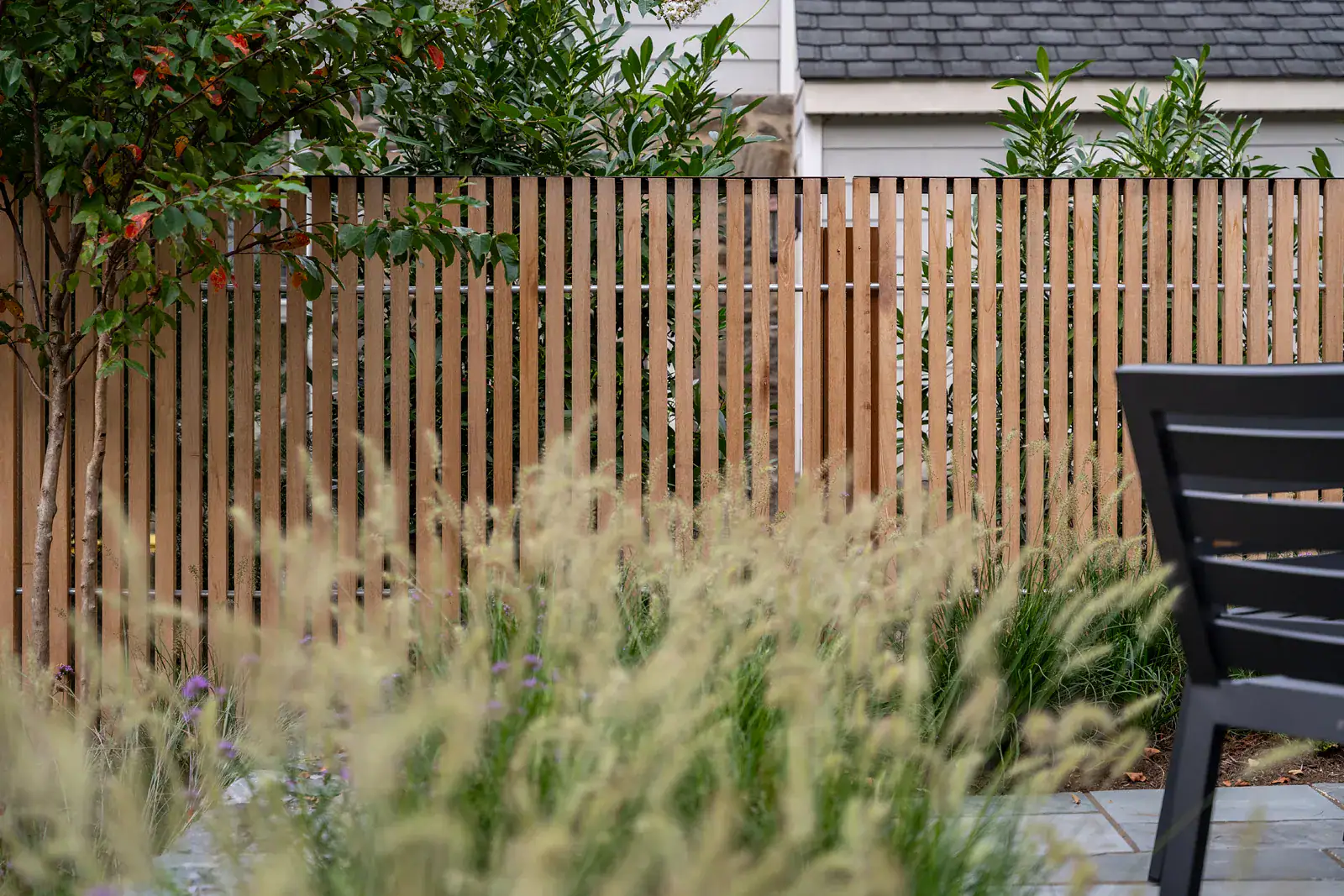 Custom cedar privacy fence with vertical slat detail, ornamental grass planting border, and multi-stem tree screening in a residential landscape design