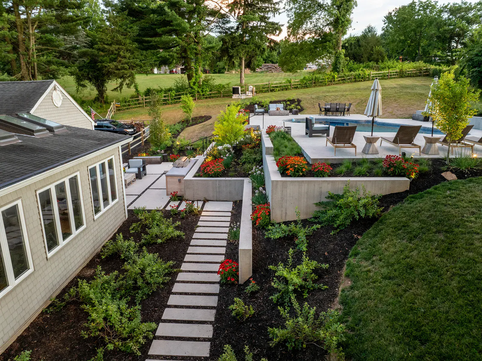 fpo-800x600 Aerial view of a Newark DE family backyard landscape design with a concrete stepping stone path rising along the home to a tiered pool terrace, board-formed concrete retaining walls, echinacea and allium beds, an outdoor kitchen, and open lawn